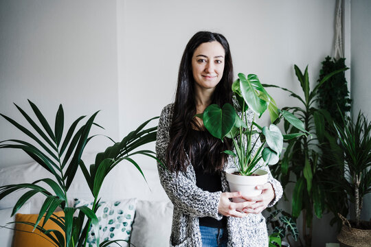 Smiling woman holding Monstera plant while standing against wall