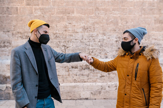 Young friends wearing protective face mask giving fist bump while standing against wall
