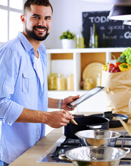 Man following recipe on digital tablet and cooking tasty and healthy food in kitchen at home - 431989193