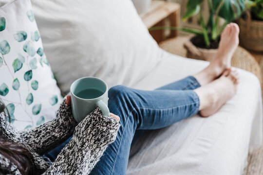Woman holding cup of water on sofa at home