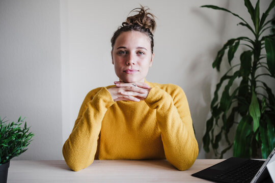 Confident woman with hand on chin staring while sitting by table at home