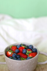 Bowl with blueberreis and strawberries and wooden tray on a bed. Selective focus.