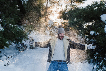 Cheerful man with arms outstretched playing on snow during winter