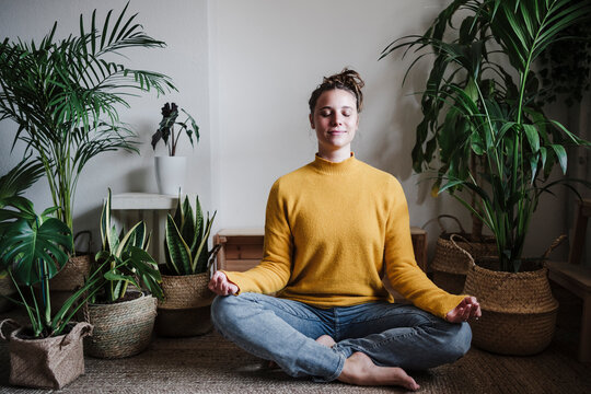 Young woman meditating while sitting on floor by plant at home