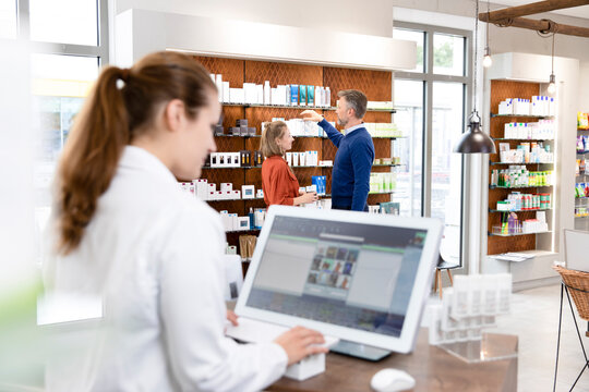 Couple taking medicine from shelf while female pharmacist using computer at pharmacy