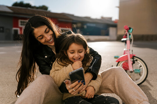 Smiling mother using mobile phone while sitting on road