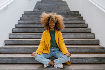 Afro woman in lotus position sitting on staircase