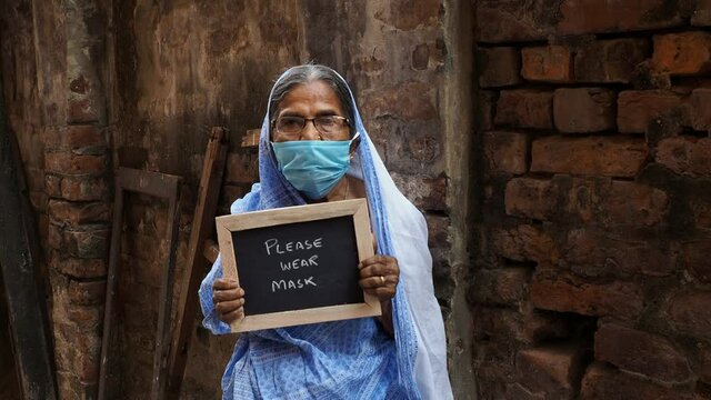 An old Indian woman with message "Please wear mask " in dark background