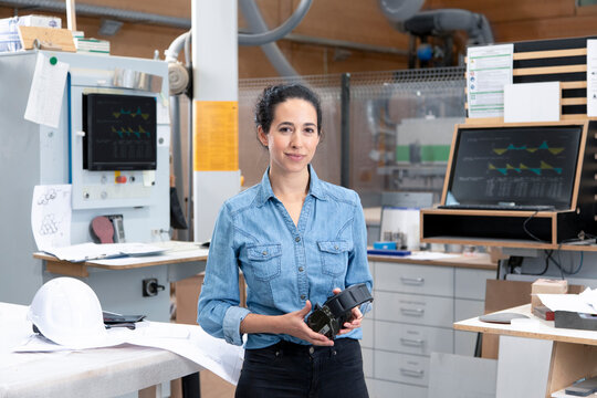 Businesswoman holding ear protectors while standing in factory
