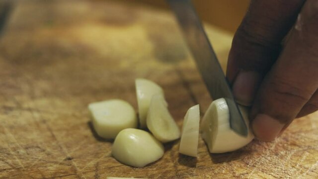 4K close-up video of mothers hands and knife slicing garlic with traditional skill in kose kitchen for home cooking shows herbal recipe for asian cuisine, especially Thai food, and also healthy food.