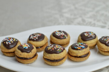 Mini traditional Austrian sandwich cookies Ischler (isleri) with chocolate and colorful sprinkles on the modern white plate, closeup