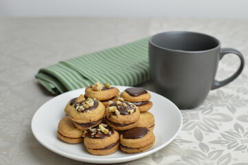 Mini traditional Austrian sandwich cookies Ischler (isleri) with chocolate and walnuts, on the white plate and cup of coffee 