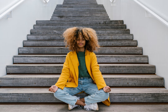 Afro woman meditating while sitting on staircase