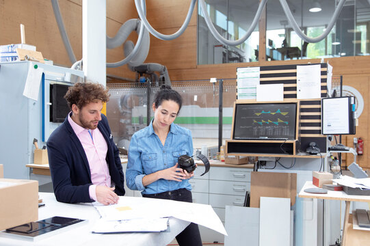 Male entrepreneur explaining strategy to female colleague holding ear protectors in factory