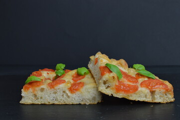 Italian focaccia  bread with tomatoes and basil, two pieces, on the dark background