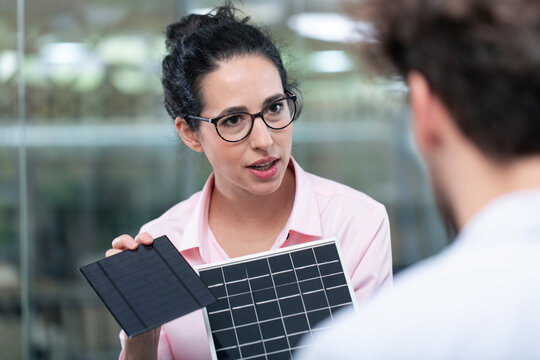 Businesswoman with eyeglasses showing solar panel model to male colleague in office