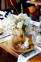 Wedding decor of roses, gypsophila and candles on a laid festive table with glasses and plates with cards. Off-season rustic wedding dinner. Blurred background and selected focus.
