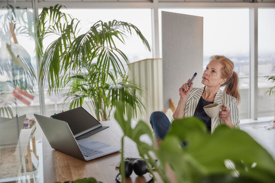 Businesswoman holding coffee cup while doing business plan at desk in office