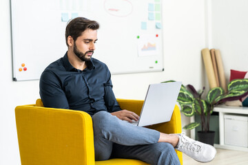 Male entrepreneur working on laptop while sitting on chair in office