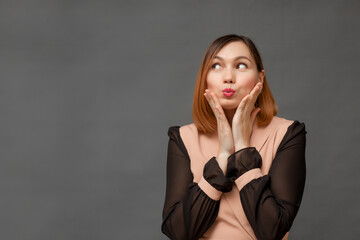Fototapeta premium a young woman looks at the camera with interest and surprise, raising her eyebrows and looking silly, standing on a gray background.