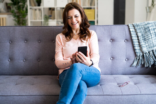 Smiling mature woman using mobile phone while sitting on sofa at home