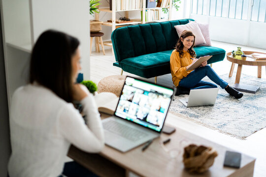 Young woman with laptop sitting at table while mother checking bills at home