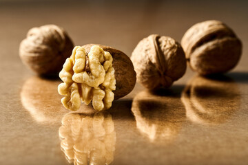 half a peeled walnut with three whole nuts on a brown background with close-up reflection