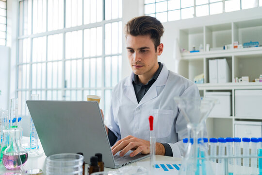 Serious male scientist working on laptop while sitting at desk in laboratory