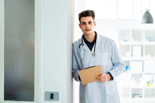Male doctor with clipboard leaning on wall in hospital