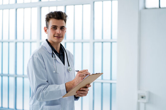 Young doctor writing notes while holding clipboard in hospital