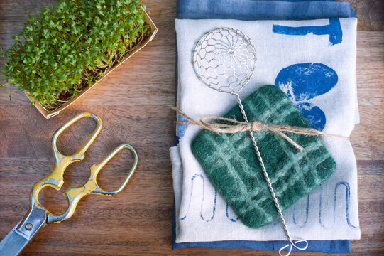 Potted watercress, pair of old scissors, sieve, dish towel covered in various prints and coaster made of felt