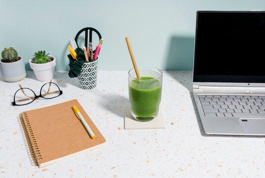 Laptop, healthy green juice, book and succulent plant over desk