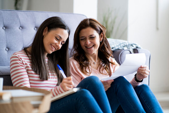 Smiling mother and daughter checking bills while sitting by sofa in living room
