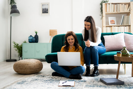 Mother with laptop and daughter sitting at sofa in living room