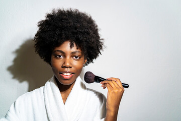 Curly woman using blushbrush while standing against white background