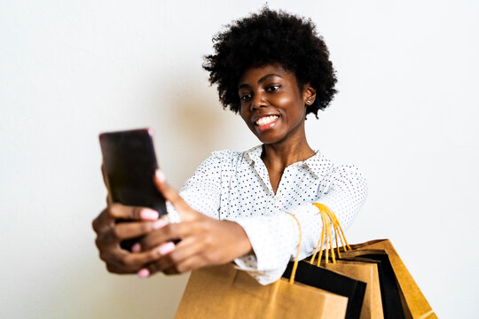 Smiling woman taking selfie through mobile phone while standing against white background