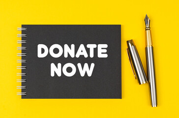 On a yellow background lies a pen and a black notebook with the inscription - Donate Now