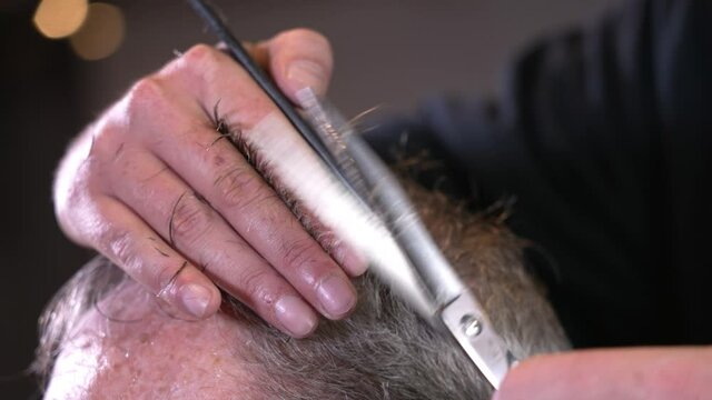 A closeup view of a barber cutting a gentleman's hair.  	