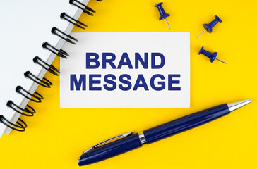 On a yellow background lies a notebook, a pen and a business card with the inscription - BRAND MESSAGE