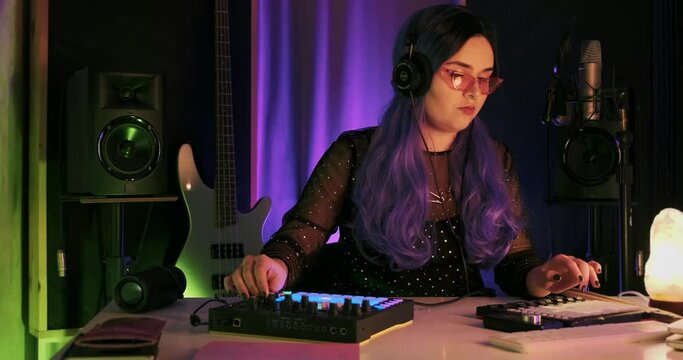 Young punk hipster girl, DJ pop house music electronic producer playing live streaming on launchpad synths in the colorful neon light home studio, bass techno production, sound designer in slow motion