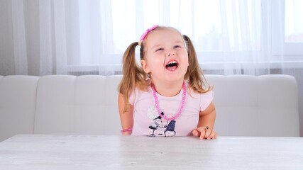 portrait of a pretty cute laughing girl 3-4 years old with big eyes and a beautiful hairstyle with a pink bow, laughing child, beads and other decorations.