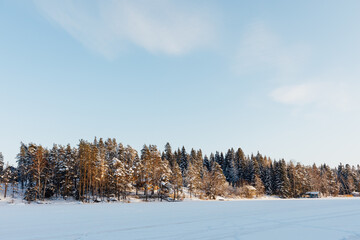 frozen lake with snow and winter forest, blue sky background
