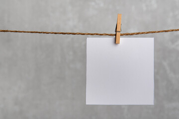One blank square note paper card hanging with wooden clip on rope string peg. Copy space, mockup