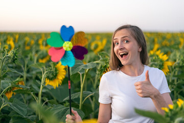 Cheerful girl holding windmill toy on field of sunflowers background. Green energy concept