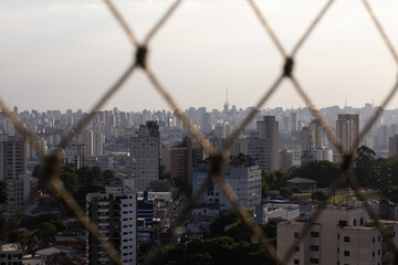 prédios da cidade retratados de dentro do apartamento com a tela de proteção da janela em...