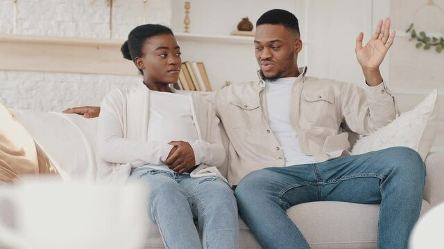 Afro american serious married couple family future parents african pregnant woman and black ethnic husband sitting on home sofa living room interior talking discussing plan about unborn baby pregnancy