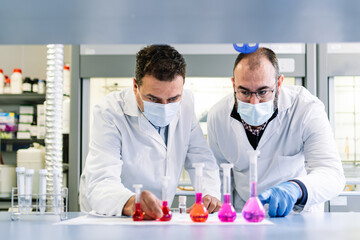 Group of two scientists studying the reaction of a chemical product in glass flasks. horizontal photography