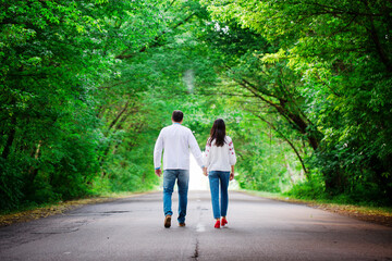 A man and a woman are walking along the road. Back view