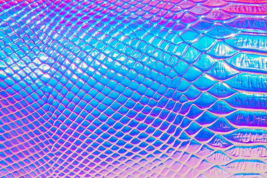 Abstract background with holographic bright rainbow multicolor. Metallized macro close up. Imitation of rainbow color. Background with a reptile skin texture in pink and blue toned