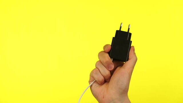 Hand holding a power plug smartphone, charging on yellow background